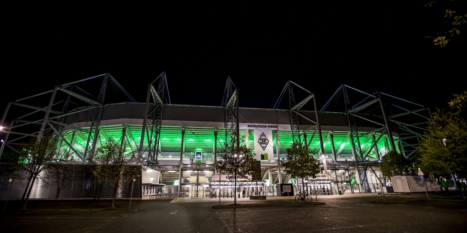 Stadion BORUSSIA-PARK in Mönchengladbach aus der Außenansicht bei Nacht, es ist innen beleuchtet. Viele grüne Linien an der Glasaußenfassade lassen die Arena grünlich aufleuchten.