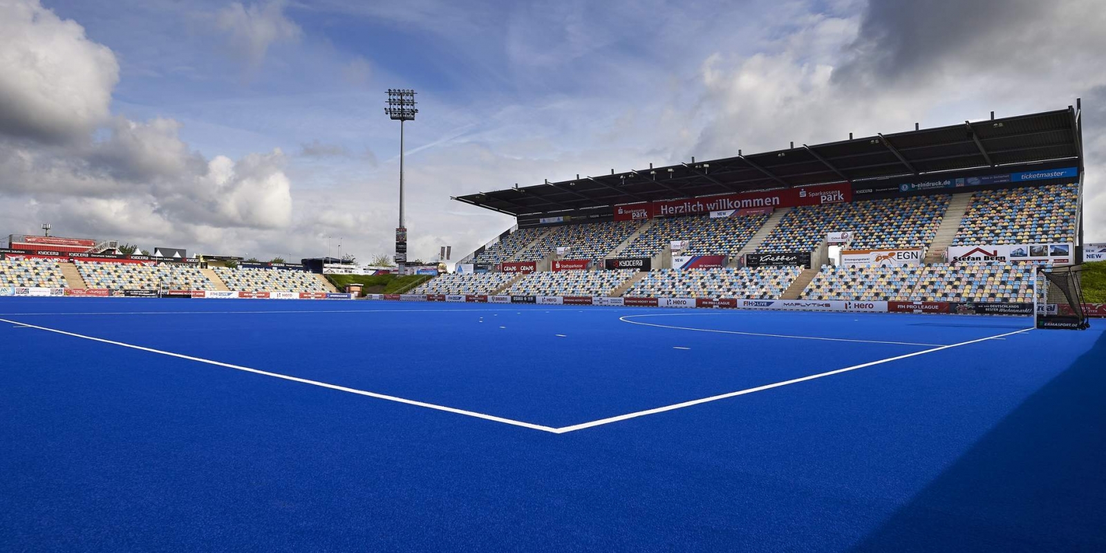 Hockeystadion SparkassenPark  Mönchengladbach aus der Innenansicht. Die Spielfläche ist blau mit weißen Begrenzungslinien, die Tribühnen teilweise überdacht.