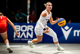 Spielerin in weißem Trikot dribbelt einen Ball in einer Halle