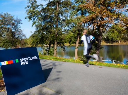 Sportland.NRW-Schild mit vorbeilaufendem Jogger