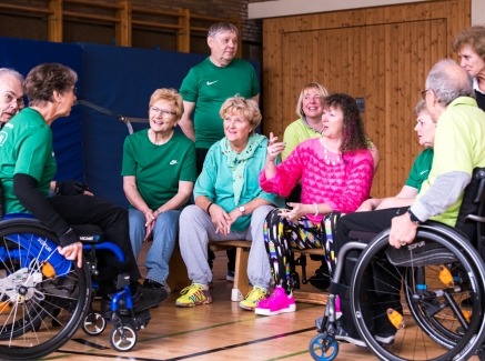 Staatssekretärin Milz sitzt mit mehreren Sportlern in einer Sporthalle. Links sitzt eine Dame im Rollstuhl, rechts ein Herr im Rollstuhl.