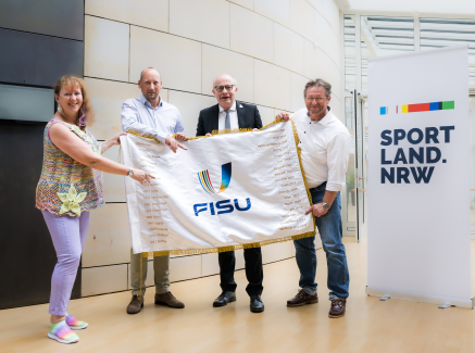 Andrea Milz mit Personen und FISU-Flagge