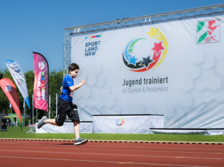 Läufer auf roter Tartanbahn vor einem Banner von Jugend trainiert