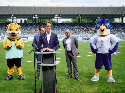 Hendrik Wüst auf dem Rasen im Lohrheidestadion mit Maskottchen und zwei Personen