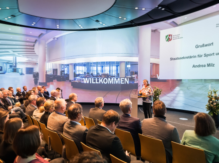 Andrea Milz auf einer Bühne mt Sitzreihen voller Personen