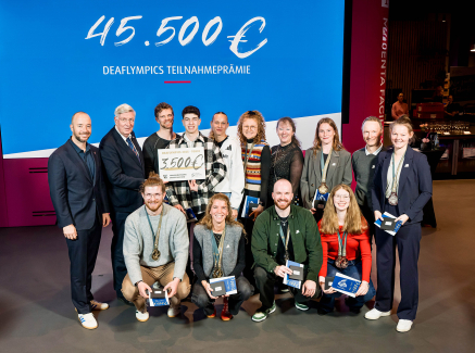 Mehrere Personen in zwei Reihen hintereinander vor einem großen blauen Banner mit 45.500 Euro