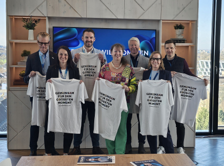 Mehrere Personen halten helle T-Shirts hoch, im Hintergrund ein Fenster