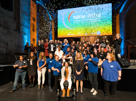 Bühne mit vielen Frauen und Mädchen, dahinter ein Bildschirm "NRW-Preis"
