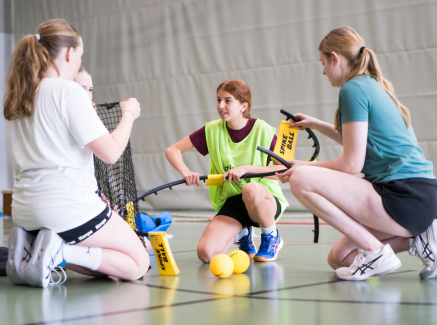 Junge Frauen in einer Halle in einem Kreis, sie bauen einen Spikeball zusammen
