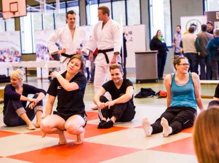 Gruppe von jungen Frauen und Männern in einer Sporthalle, einige in Judo-Dress