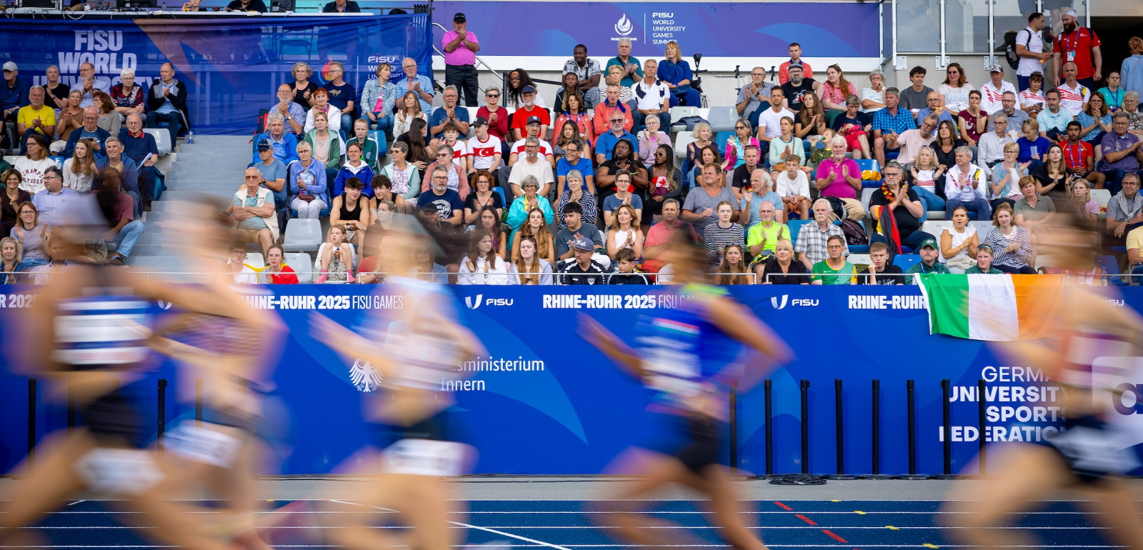 Sportlerinnen in einem Stadion laufen vor voll besetzter Zuschauertribüne