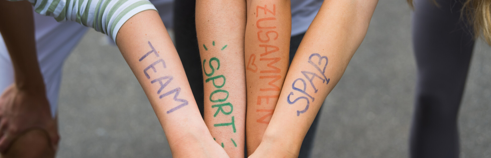 Vier Unterarme mit Schriftzügen Team, Sport, Zusammen, Spaß