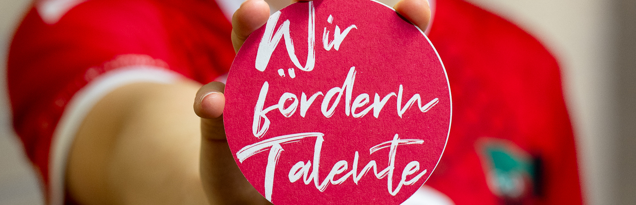 Junge Sportlerin in rotem Shirt hält Plakette in die Kamera