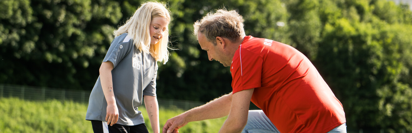 Junger Übungleiter kniet vor einer jungen Sportlerin und erklärt etwas