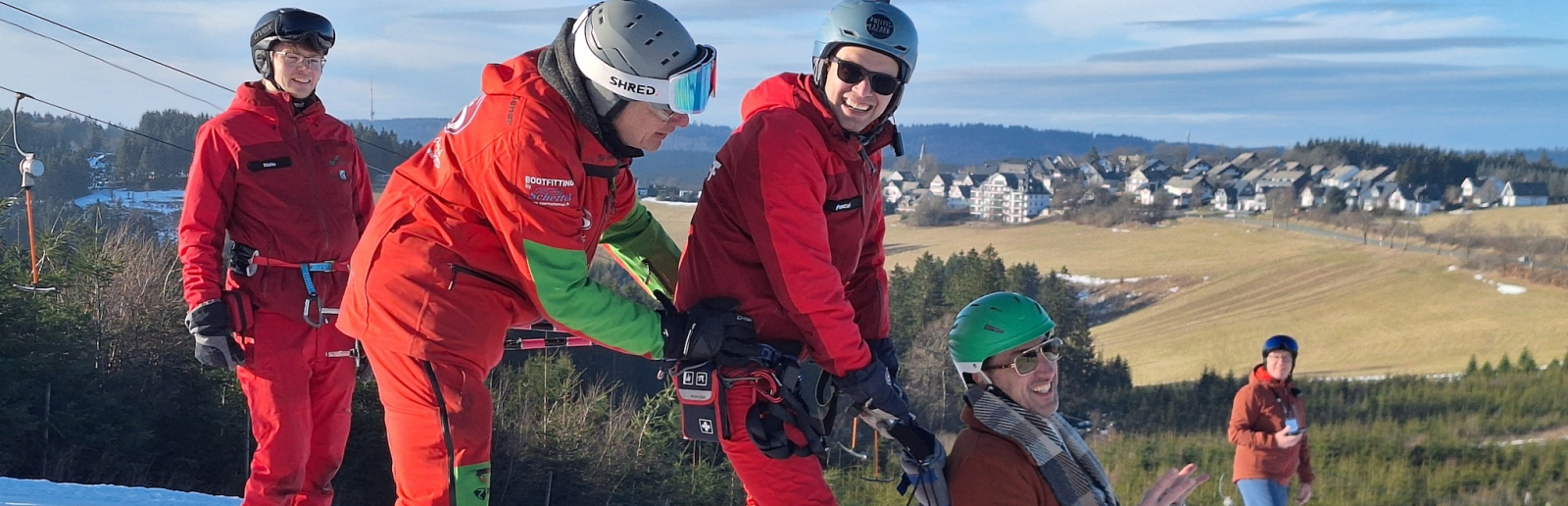 Wintersportler mit roten Anzügen schieben eine Person in einem Schlitten