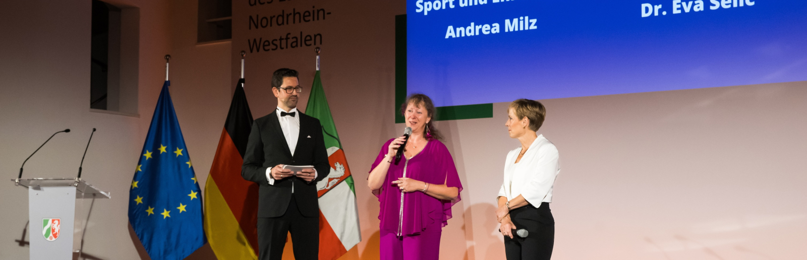 Bühne mit Redner, Andrea Milz und Eva Selic 