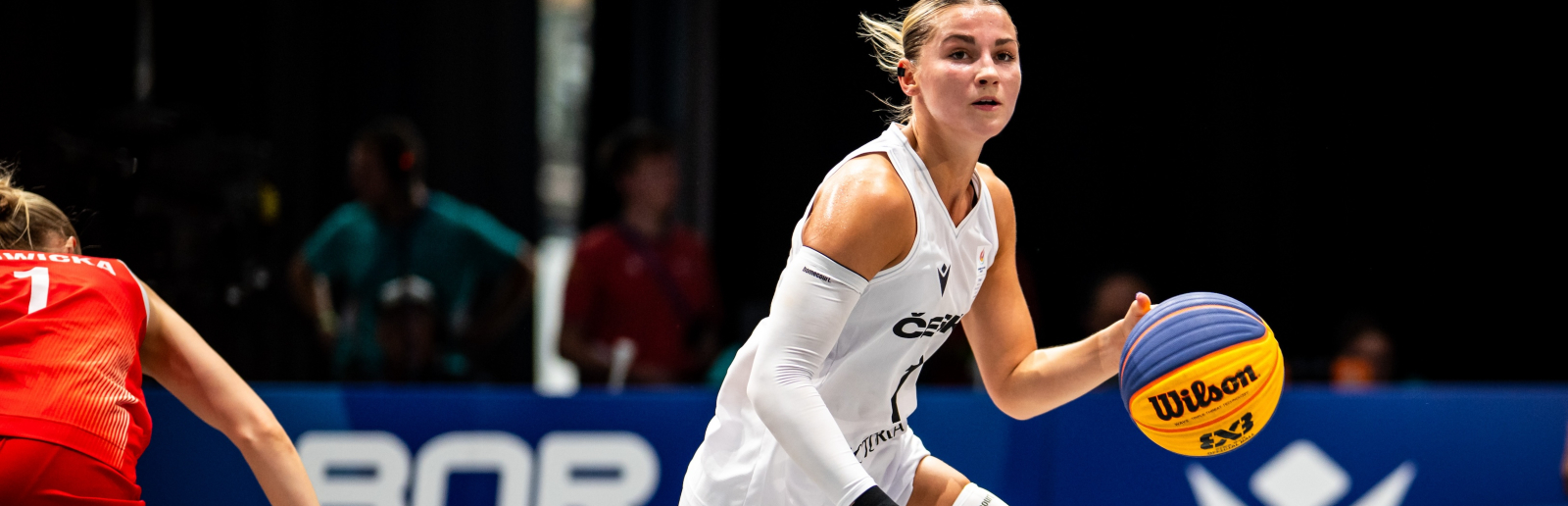 Spielerin in weißem Trikot dribbelt einen Ball in einer Halle