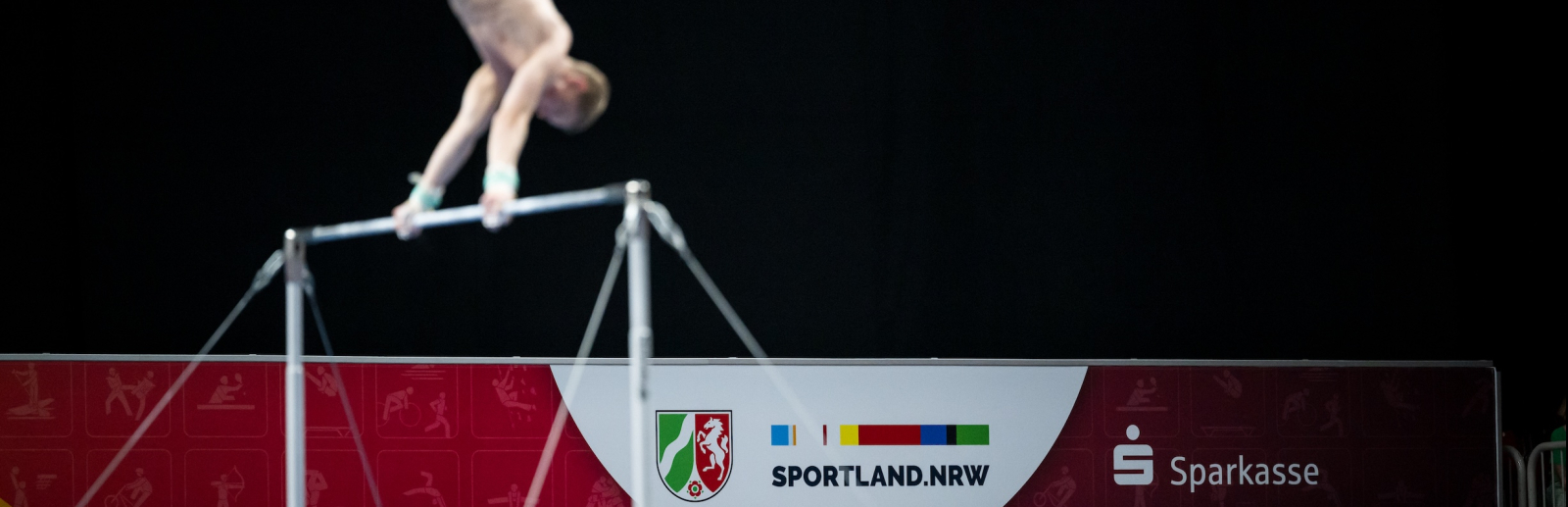 Geräteturner am Reck mit Schriftzug Sportland.NRW auf einem Banner im Hintergrund