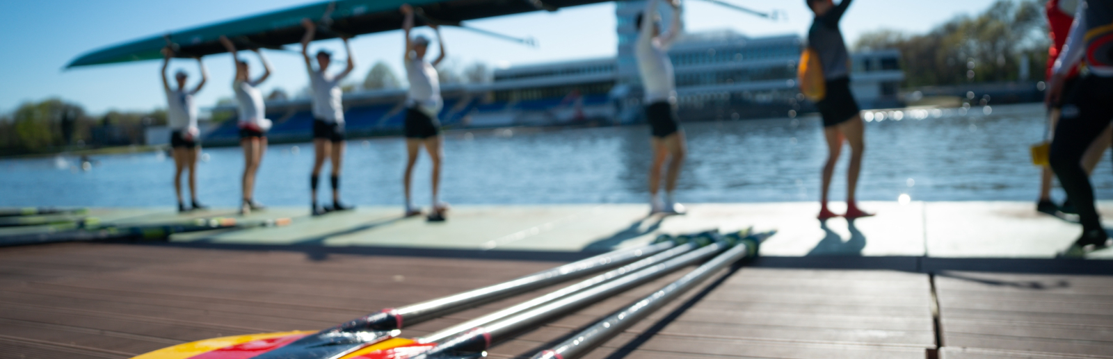 Ruderer mit dem Boot über dem Kopf, im Vordergrund Ruderblätter in den Deutschland-Farben