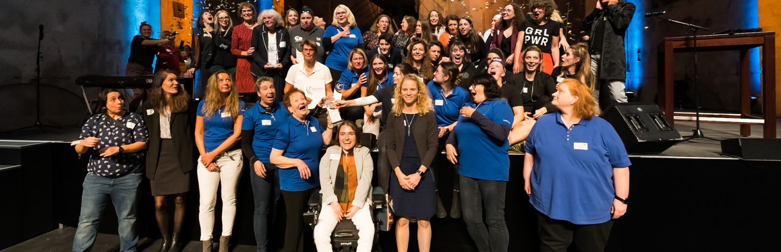 Bühne mit vielen Frauen und Mädchen, dahinter ein Bildschirm "NRW-Preis"
