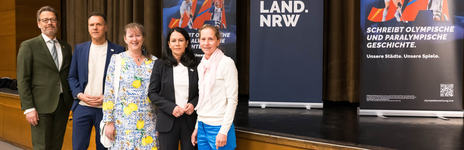 Andrea Milz und weitere vier Personen vor einer Bühne mit Aufstellern zur Bewerbung KölnRheinRuhr