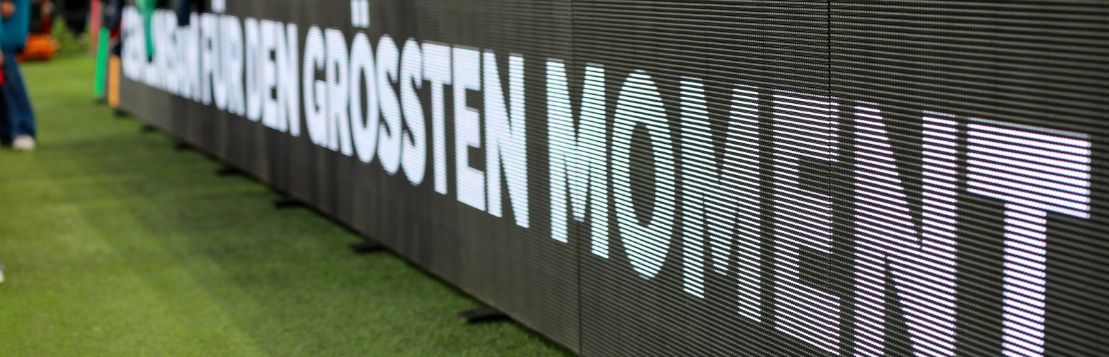 Auf einer Bande am Fußballball-Spielfeldrand steht "für den größten Moment"