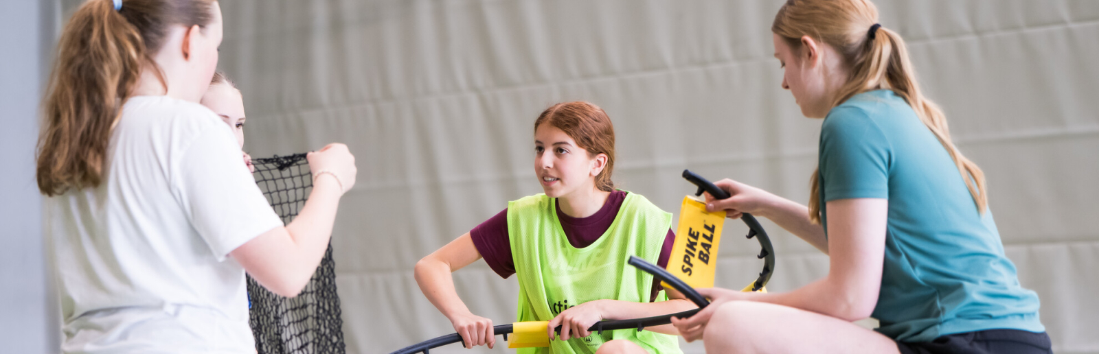 Junge Frauen in einer Halle in einem Kreis, sie bauen einen Spikeball zusammen