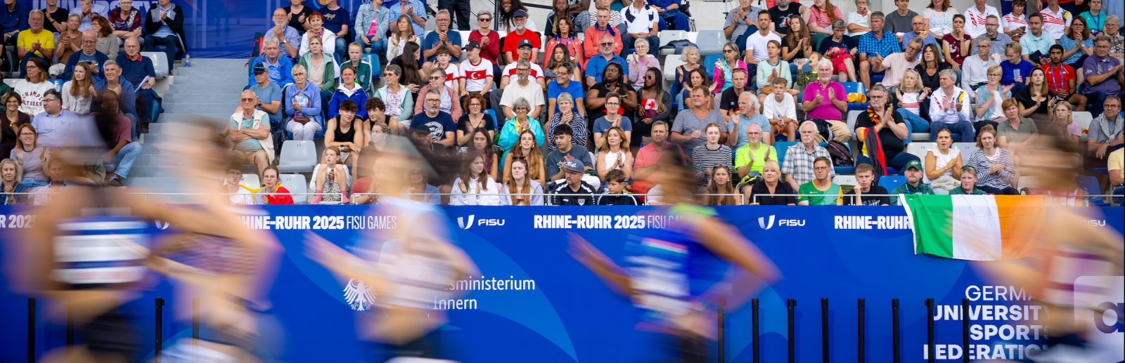 Sportlerinnen in einem Stadion laufen vor voll besetzter Zuschauertribüne