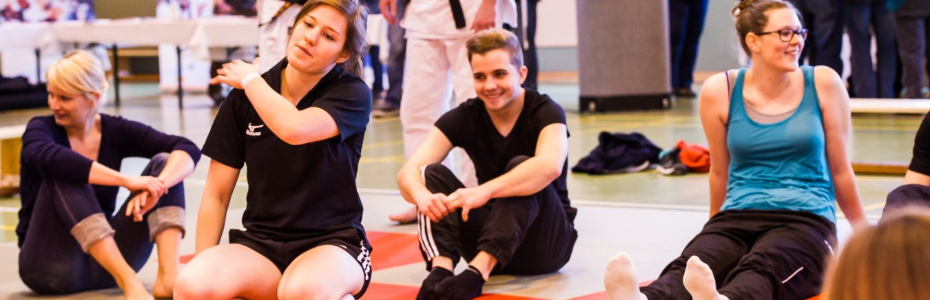 Gruppe von jungen Frauen und Männern in einer Sporthalle, einige in Judo-Dress