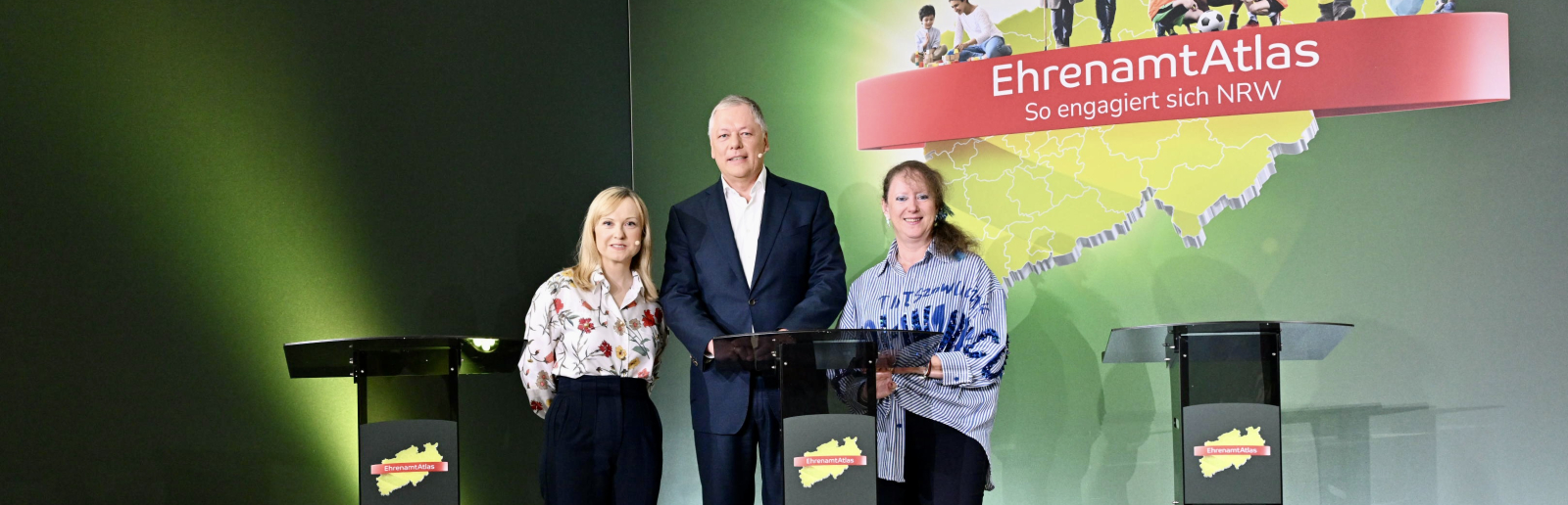 Zwei Frauen und ein Mann stehen hinter Rednerpulden