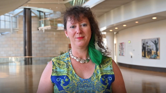 Staatssekretärin Milz in einem blau-grünem Kleid steht in einem großen Foyer, rechts an der Wand hängen einige Kunstgemälde.
