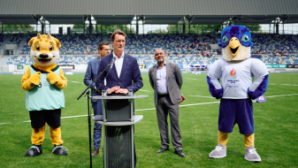 Hendrik Wüst auf dem Rasen im Lohrheidestadion mit Maskottchen und zwei Personen