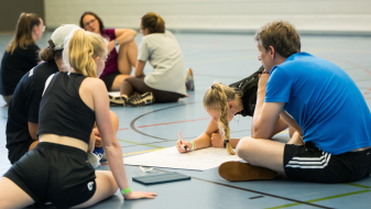 Junge Menschen in einer Sportalle beugen sich über ein Papier