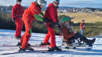 Wintersportler mit roten Anzügen schieben eine Person in einem Schlitten