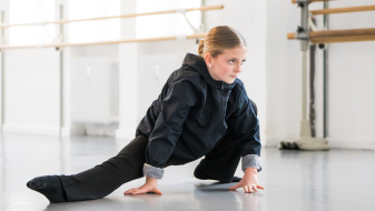 Junge Frau in dunkler Kleidung in Tanzpose mit Händen auf dem Boden in einem Studio
