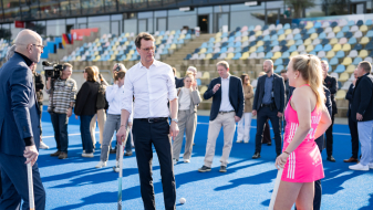 Ministerpräsident Wüst mit Hockeyschläger neben einer Hockeyspielerin in pinkem Dress im Stadion