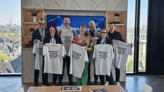 Mehrere Personen halten helle T-Shirts hoch, im Hintergrund ein Fenster