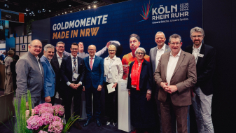 Viele Personen vor einer Wand mit Schriftzug "Goldene Momente" der KölnRheinRuhr-Bewerbung