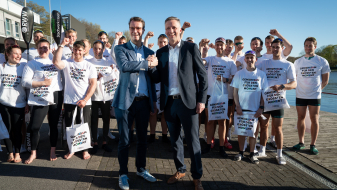 Hendrik Wüst umgeben von Ruderen in weißen Shirts mit der Aufschrift "Gemeinsam für den Größten Moment"