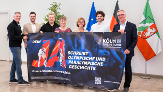 Sieben Personen, darunter Andrea Milz, halten ein Plakat zur Bewerbung KölnRheinRuhr