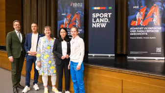 Andrea Milz und weitere vier Personen vor einer Bühne mit Aufstellern zur Bewerbung KölnRheinRuhr