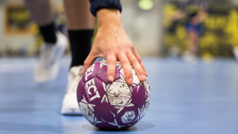 Handball auf einem blauen Boden, im Hintergrund sind Hände zu sehen