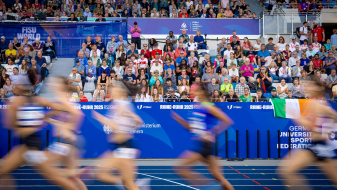 Leichtathletinnen laufen in einem Stadion vor einer vollen Zuschauertribüne