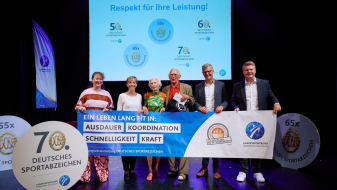 Sechs Personen halten einen Banner bei einer Veranstaltung, wo der 100-jährige Johann Otte als ältester Teilnehmer beim Deutschen Sportabzeichen ausgezeichnet wurde.