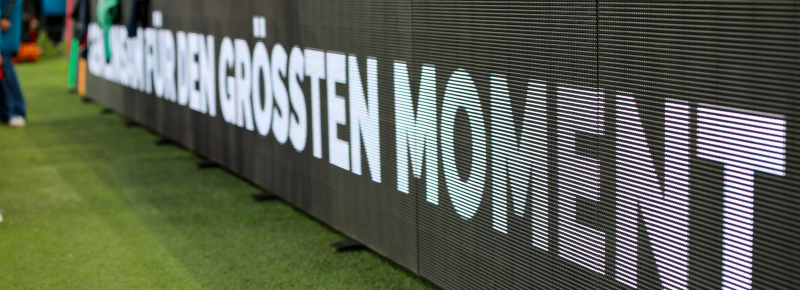 Dunkle Bande im Fußballstadion mit der Aufschrift "Für den größten Moment"