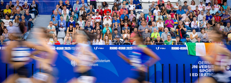 Sportlerinnen in einem Stadion laufen vor voll besetzter Zuschauertribüne