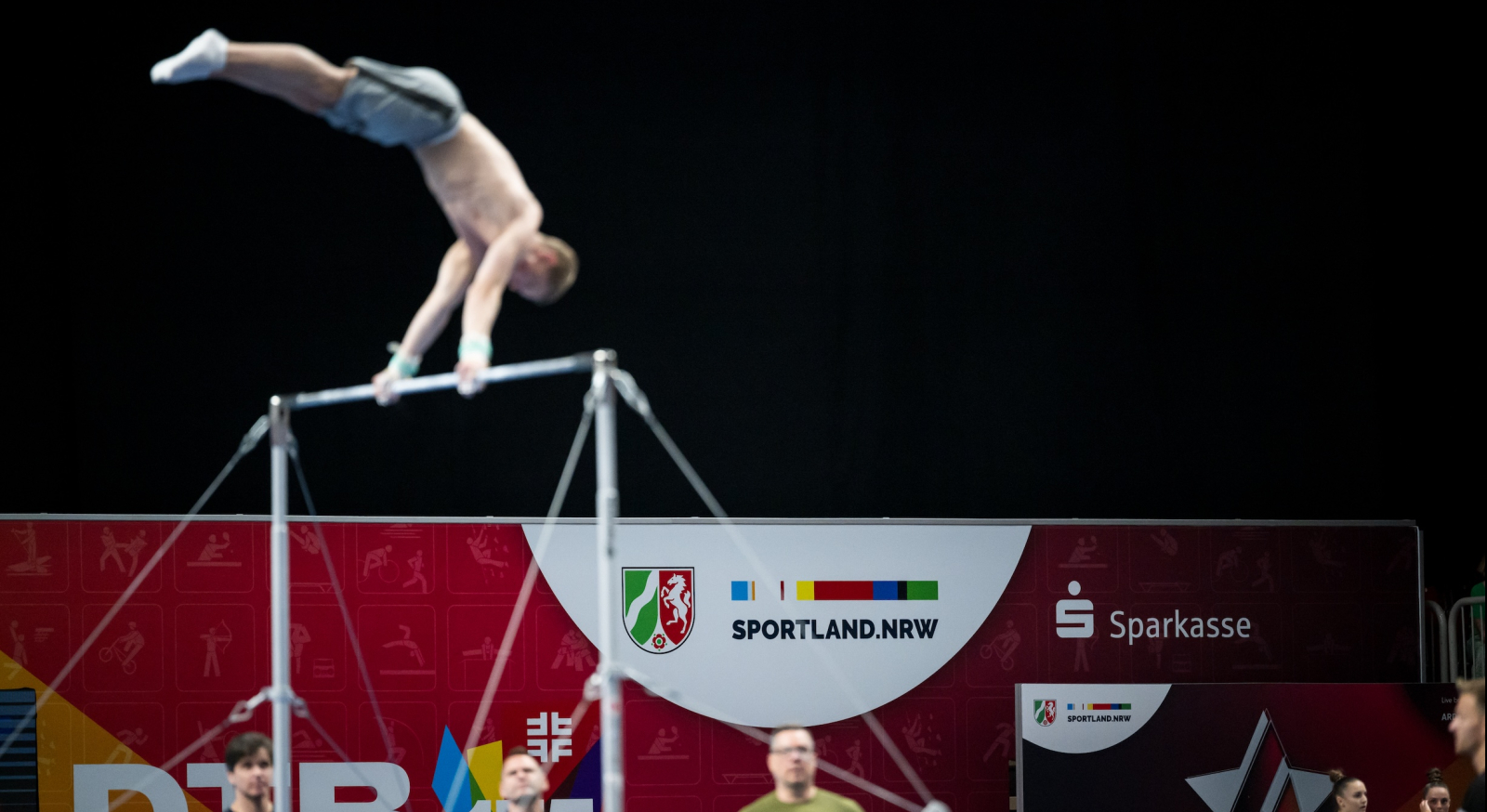 Geräteturner am Reck vor dunklem Hintergrund und Schriftzug Sportland.NRW