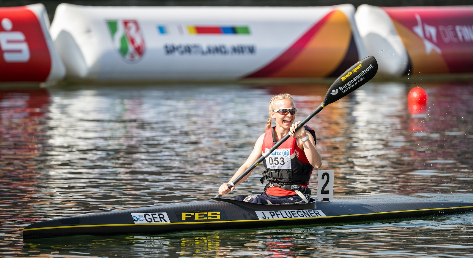 Kanufahrerin auf dem Wasser mit einem Banner "Sportland.NRW" im Hintergrund