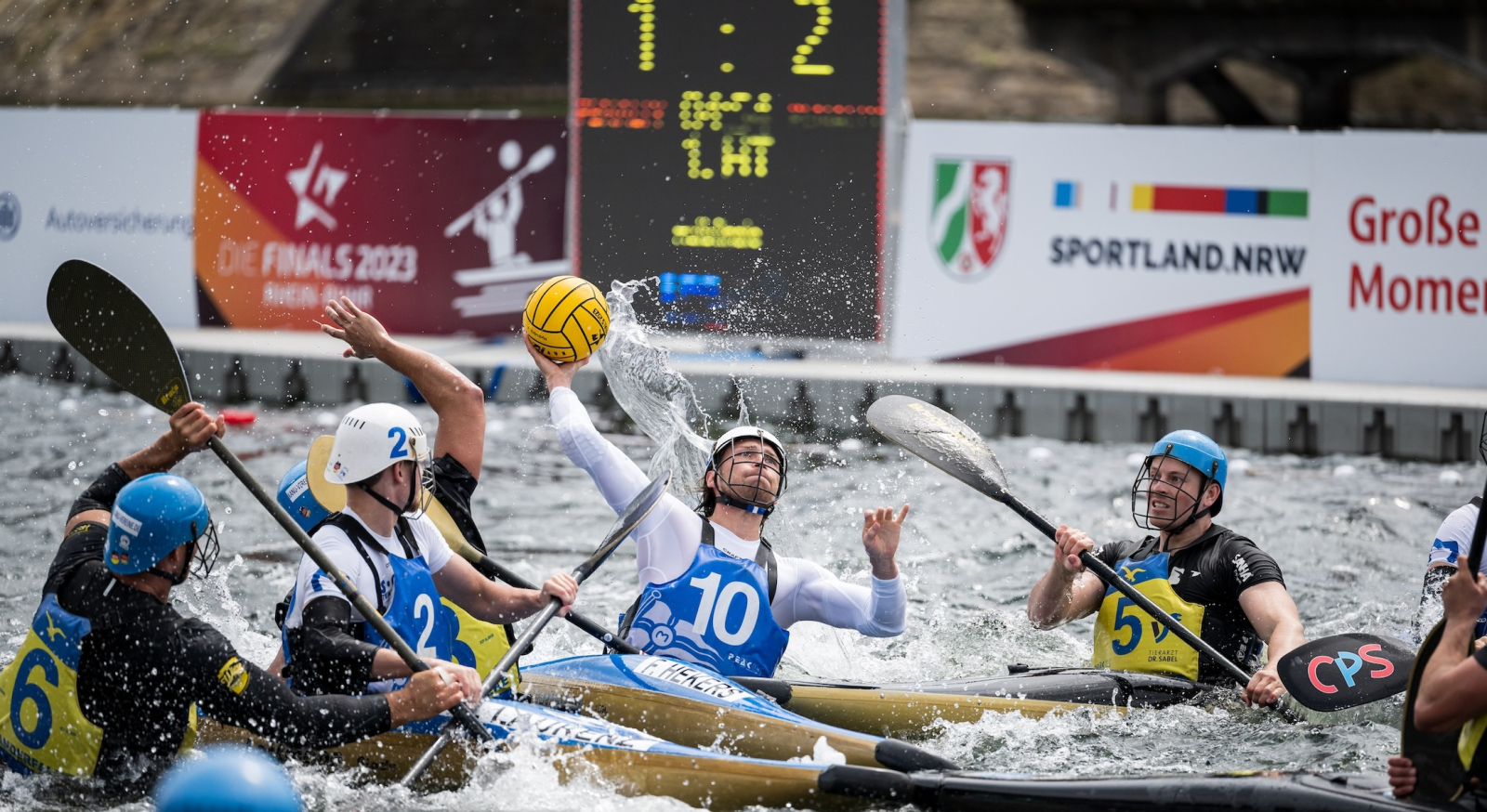 Kanu-Polo-Spieler auf dem Wasser mit einem Banner "Sportland.NRW" im Hintergrund