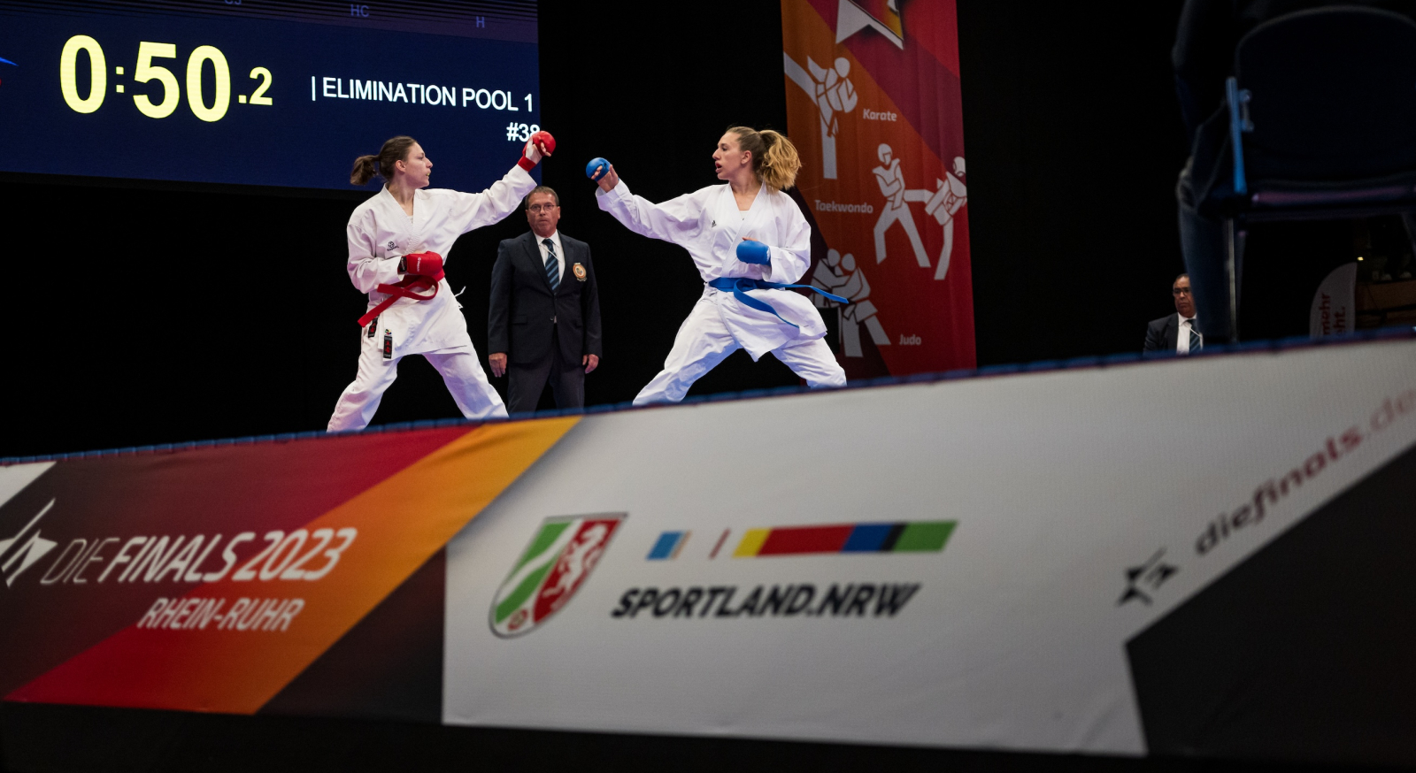 Zwei Karateka in Aktion, im Vordergrund ein Schild mit "Sportland.NRW"